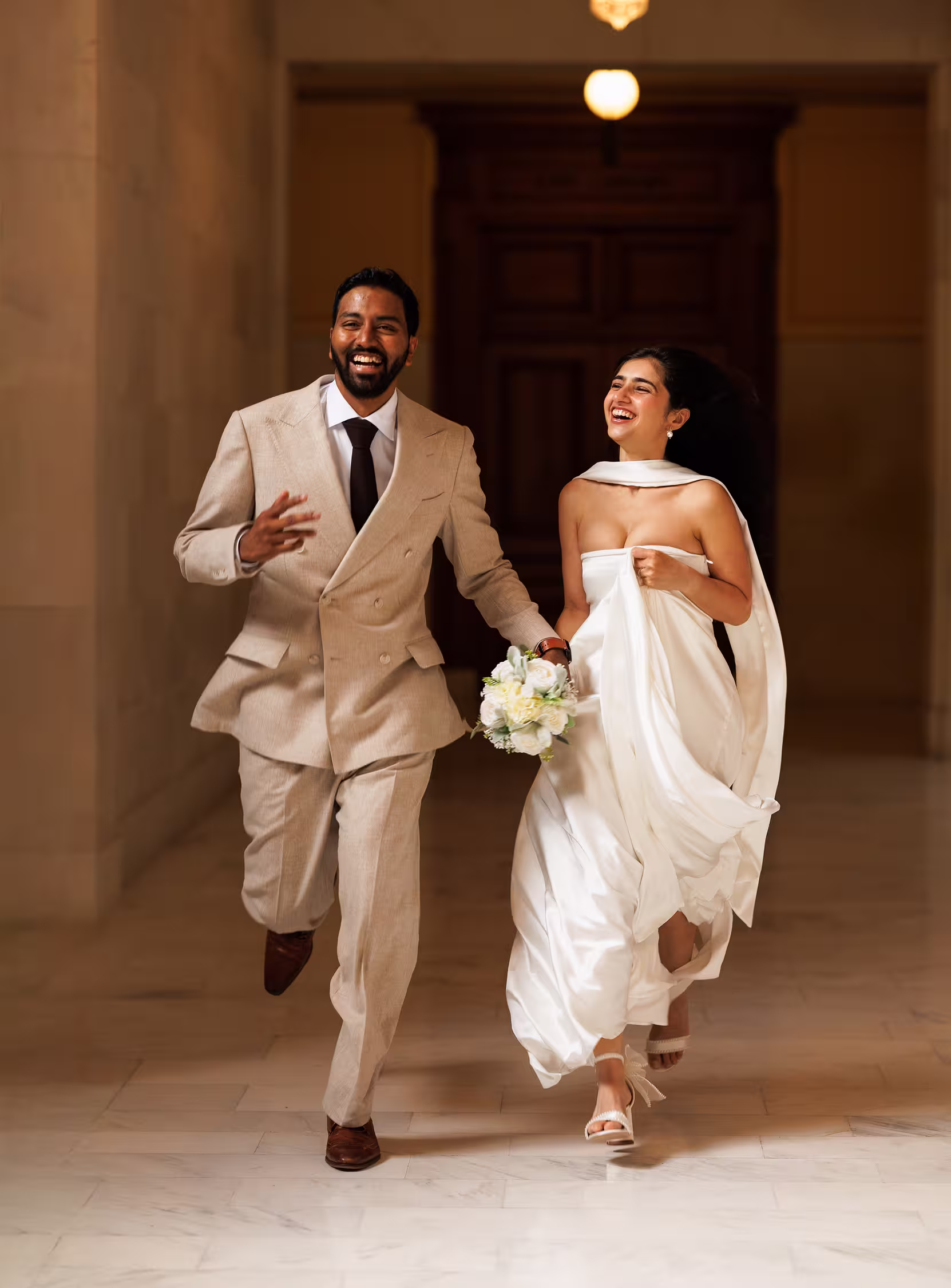 Bride and groom laughing and running through the hallway inside San Francisco City Hall, joyful candid wedding moment with elegant light and motion