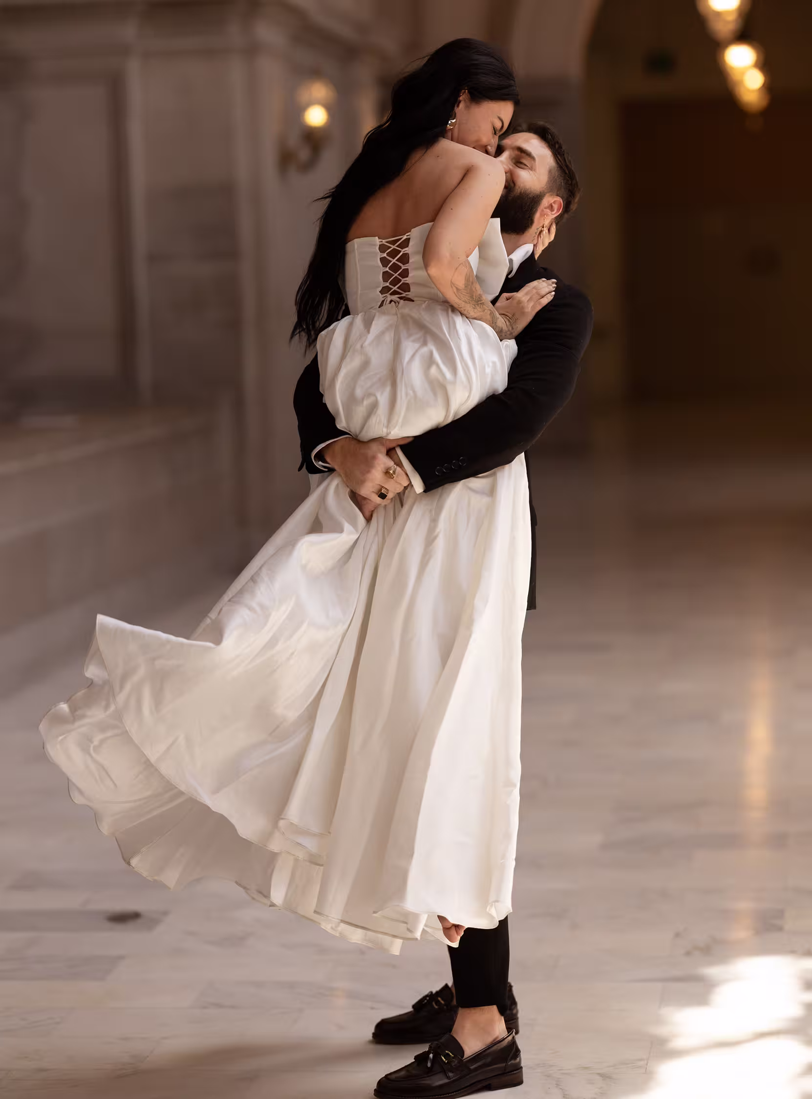 Groom lifting bride in a joyful embrace inside San Francisco City Hall, flowing dress and soft natural light in an intimate romantic moment