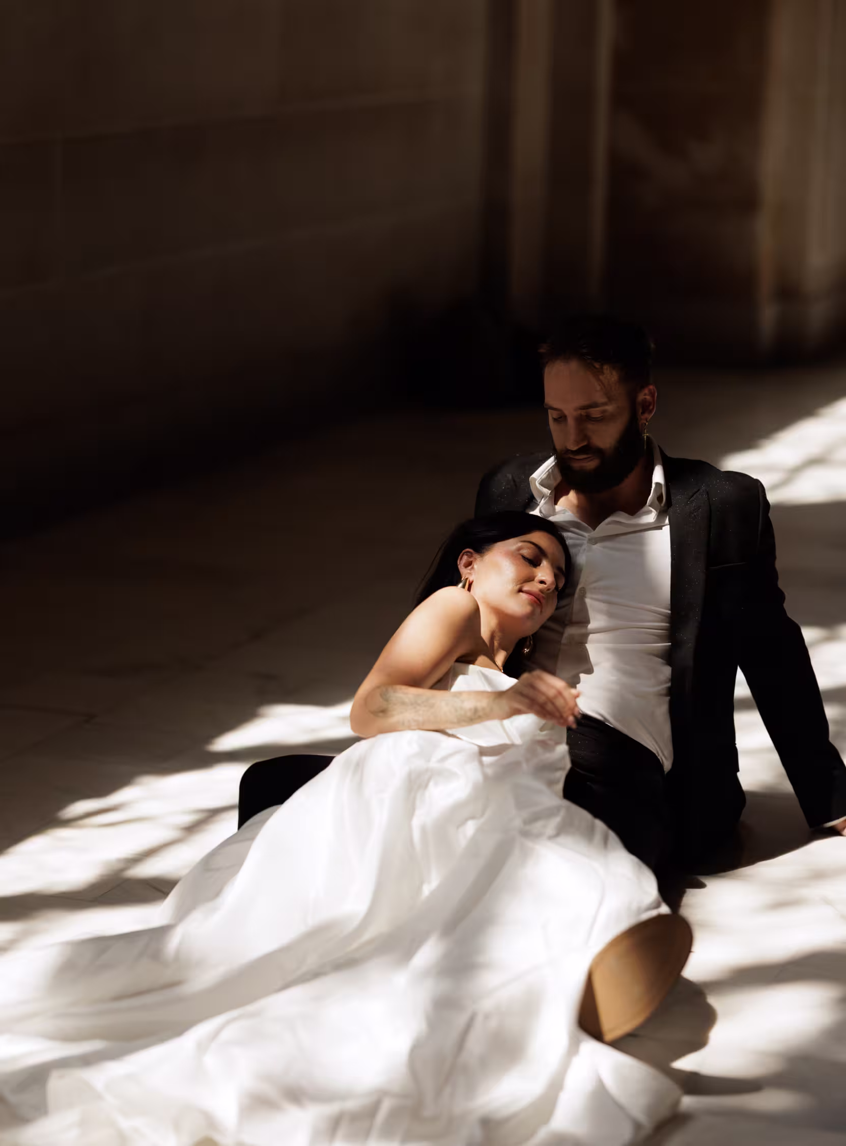 Bride resting in groom’s arms on the marble floor inside San Francisco City Hall, soft sunlight and intimate romantic moment in elegant wedding portrait