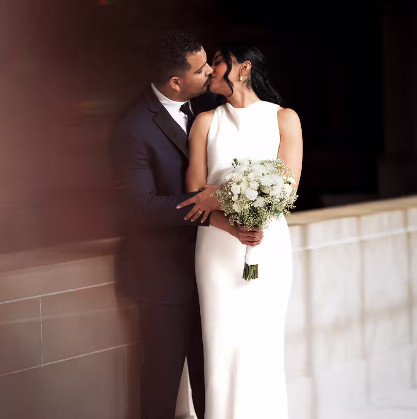 San Francisco City Hall wedding couple kissing on the balcony, bride in modern gown holding a bouquet