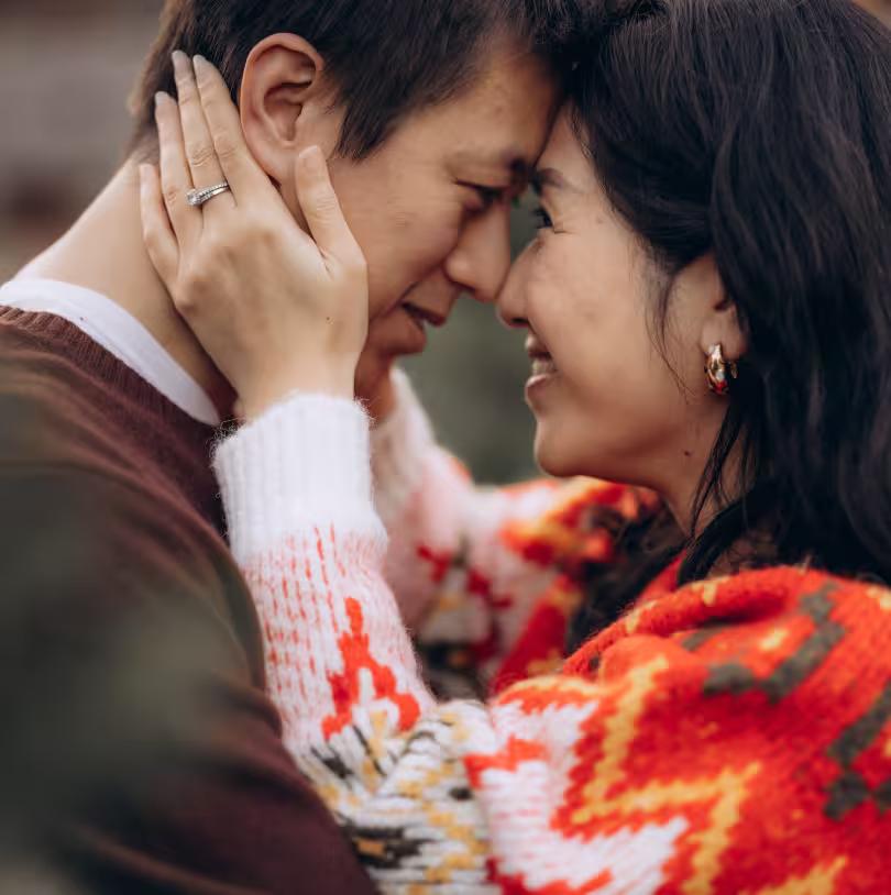 Smiling Bay Area couple in cozy sweaters touching foreheads in a warm, intimate portrait