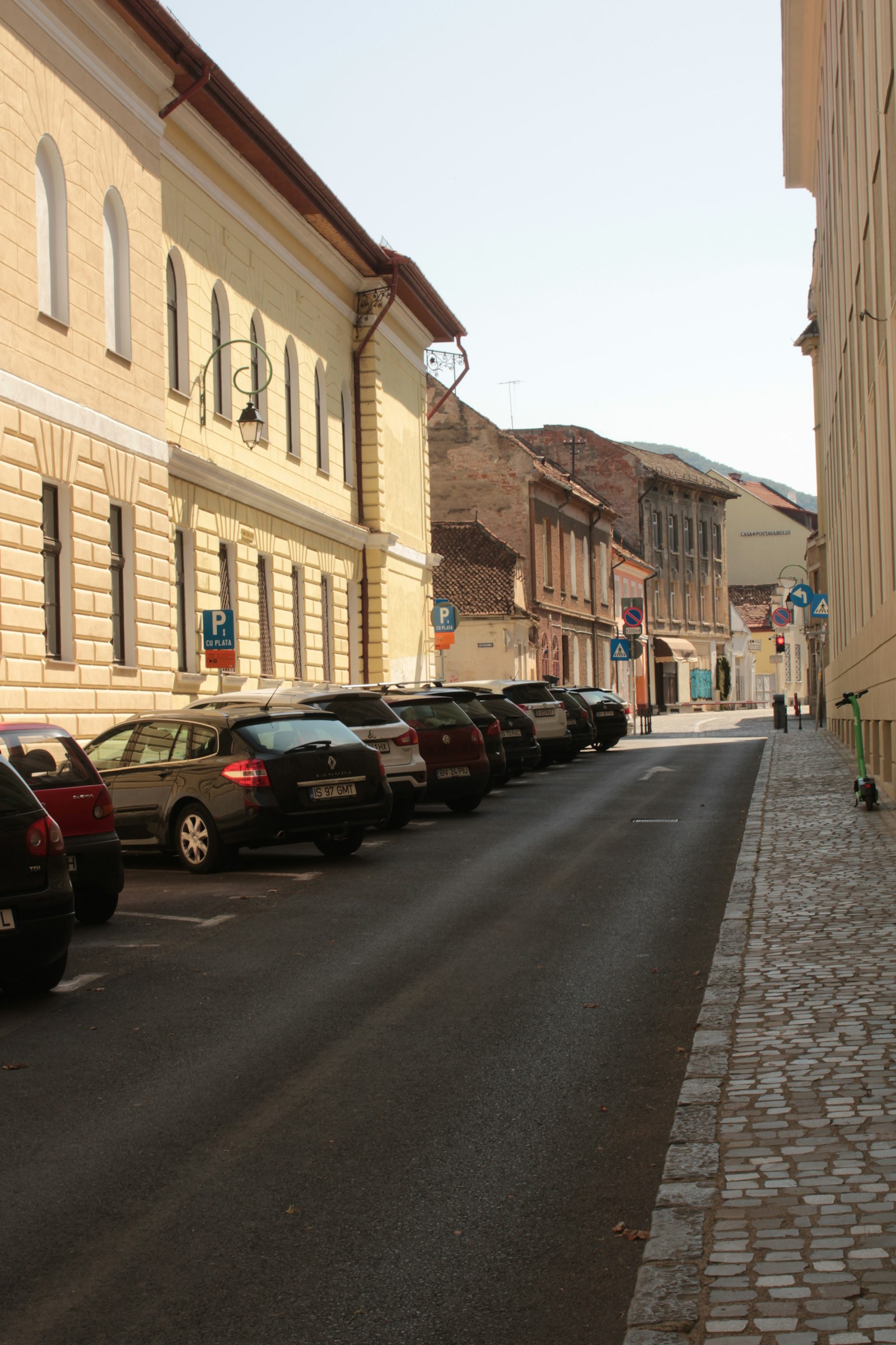 Stradă din centrul Brașovului cu mașini parcate și indicator de parcare