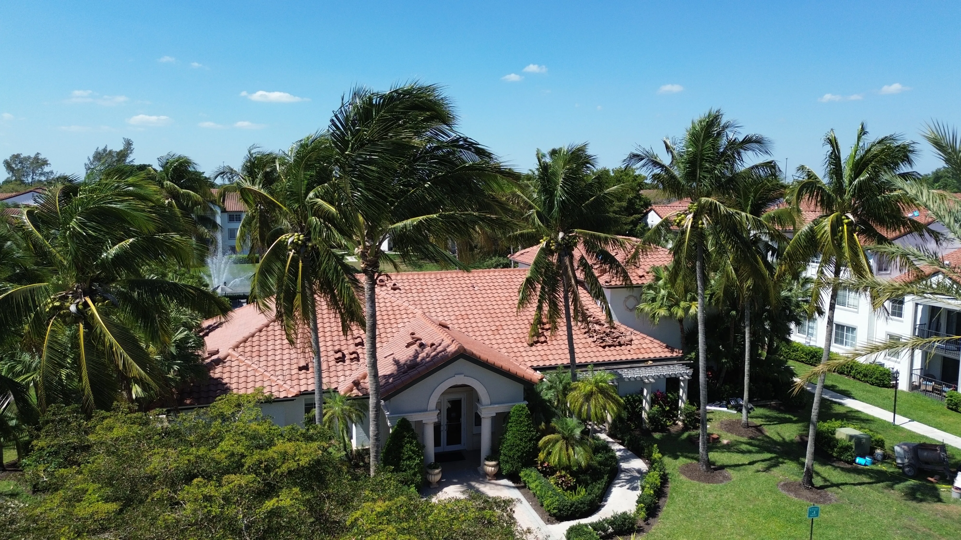 Aerial view of The Enclave clubhouse with palm trees and barrel tile roof