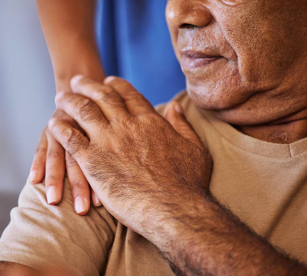 An older man patting the hand of the care aid helping him