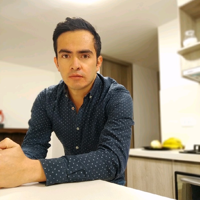 Hombre con camisa azul estampada apoyado en una encimera en una cocina moderna.