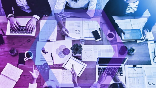 An overhead view of a diverse business team collaborating around a table filled with laptops, tablets, and financial charts. This image represents the visibility and control that Menlo Security provides to ensure app and data access policies are working correctly.