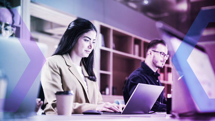 Two people working on laptops in a modern office, illuminated by soft lighting and a blue-purple overlay, illustrating the advanced technology and secure environment described in the 'Network Separation' section."
