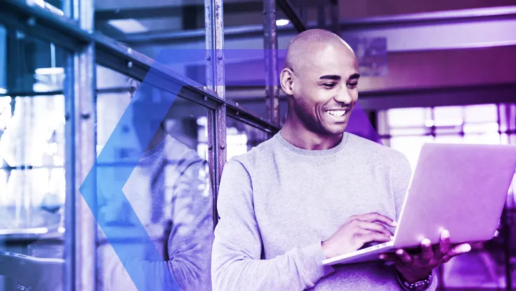 A smiling man works on his laptop in a modern, brightly lit office. This image represents the seamless and positive user experience that results from the robust 'Explicit Verification' security policies running in the background.