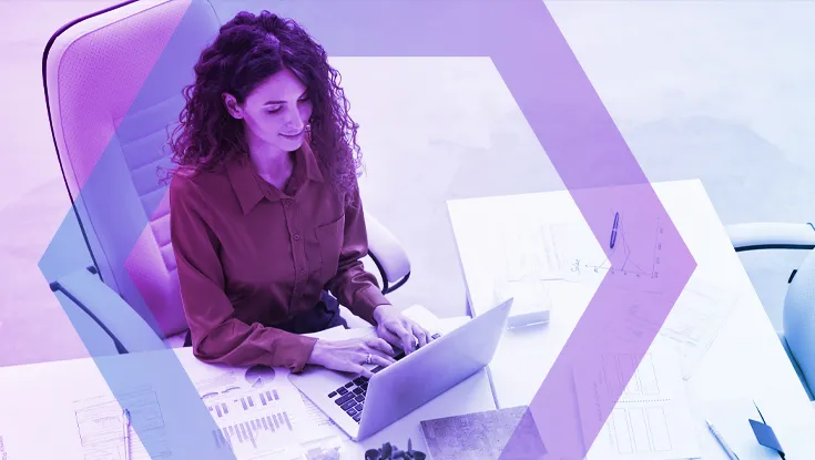 A high-angle view of a female professional with curly hair working on her laptop at a white desk. She is analyzing data charts and reports, demonstrating focused productivity in a secure environment, which is represented by a blue and purple geometric overlay.