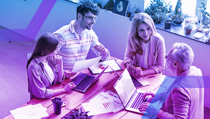 A diverse team of four colleagues collaborates around a wooden table in a business meeting. They are reviewing data on laptops and paper charts, demonstrating seamless team productivity. The scene features a blue and purple color overlay, symbolizing a secure work environment for data sharing.