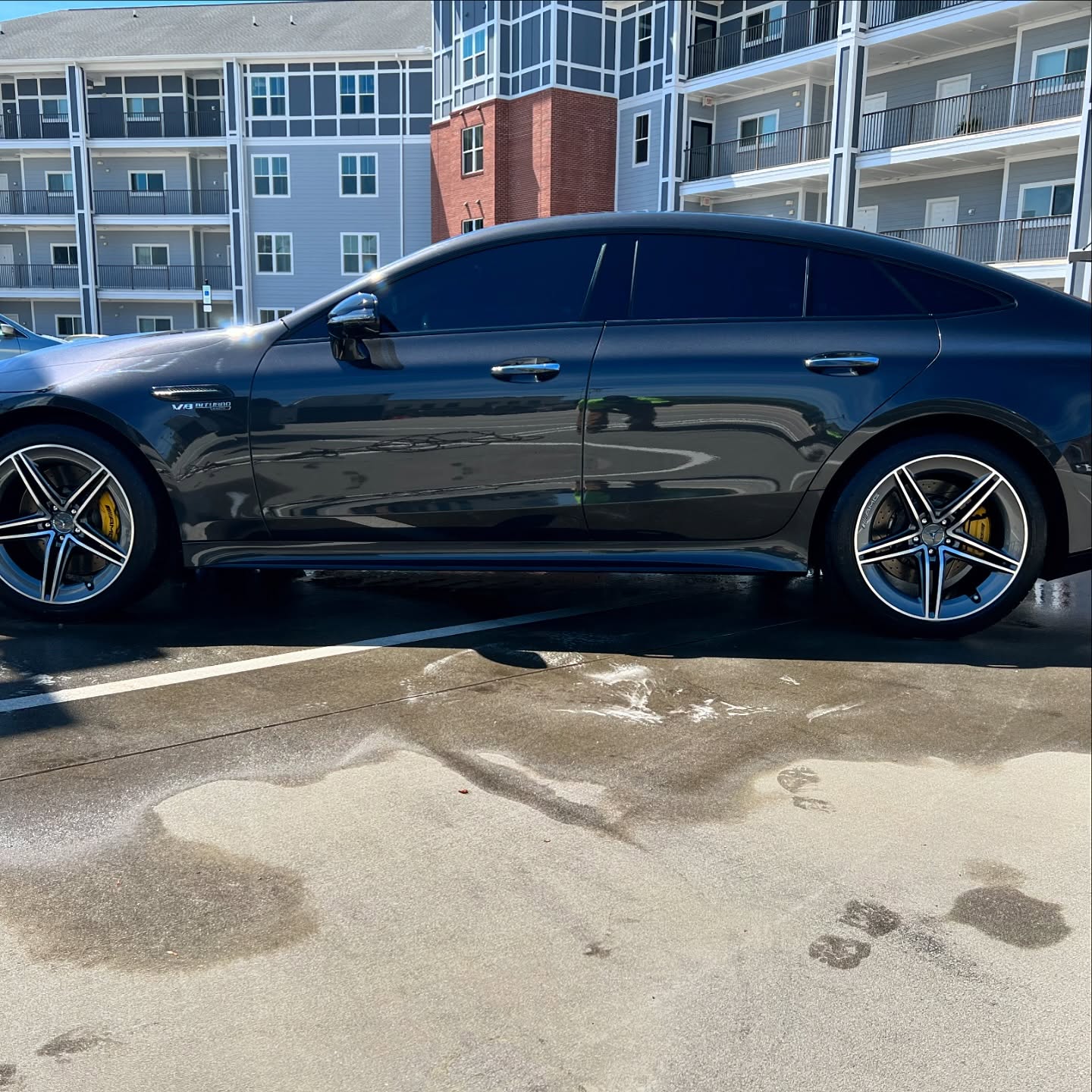 Side view of a black luxury sedan with tinted windows parked in an outdoor parking lot in front of apartment buildings.