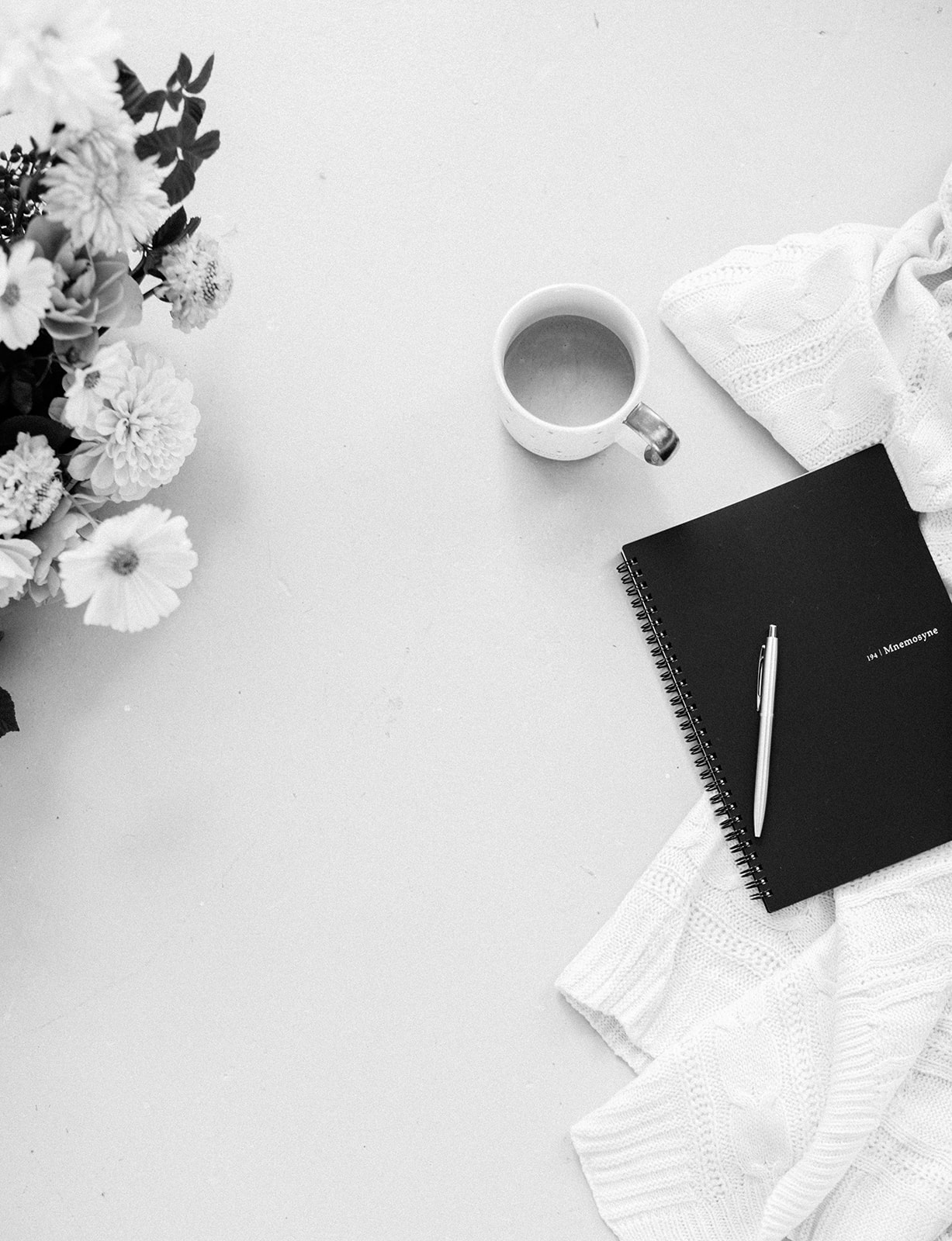 A flat lay with flowers, a coffee, and a notebook