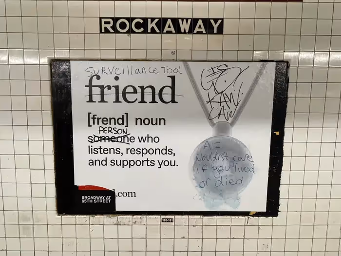 Photo of Friend AI companion subway ad at Rockaway station showing the word “friend” with its definition. The poster is heavily vandalized with phrases like “surveillance tool” and “AI wouldn’t care if you lived or died,” replacing “someone” with “person.”