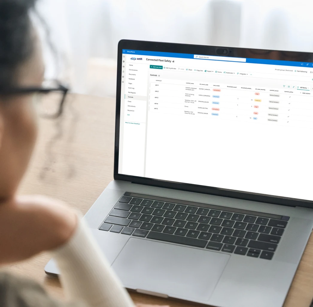Person wearing glasses viewing a laptop screen displaying a SharePoint page titled 'Connected Fleet Safety' with a controls table.