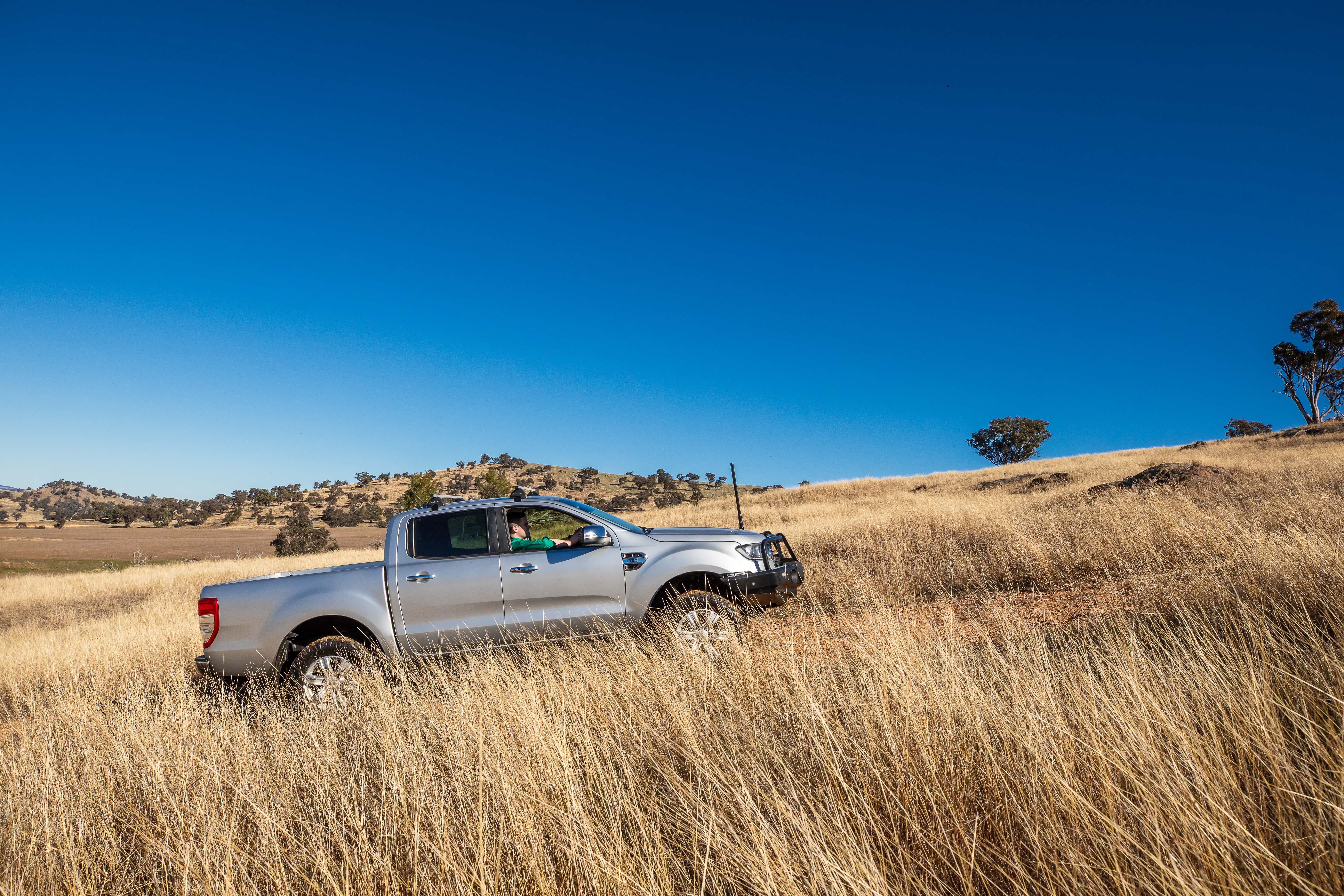 White SUV driving on a red dirt road through dense green shrubland at sunrise.