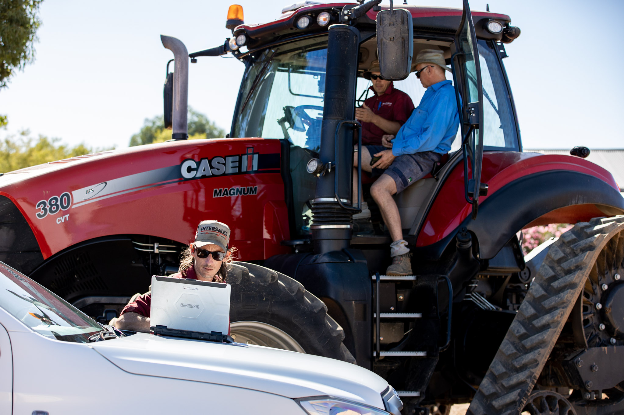 Two men sitting in a red Case IH Magnum 380 tractor, one man using a laptop on a white vehicle.