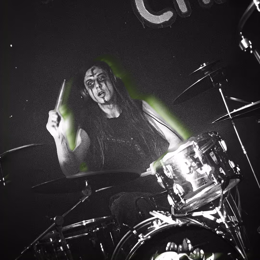 Musician with bright orange hair playing a drum set in a dimly lit studio with green lighting and a 'Bully's Studios' sign on the wall.