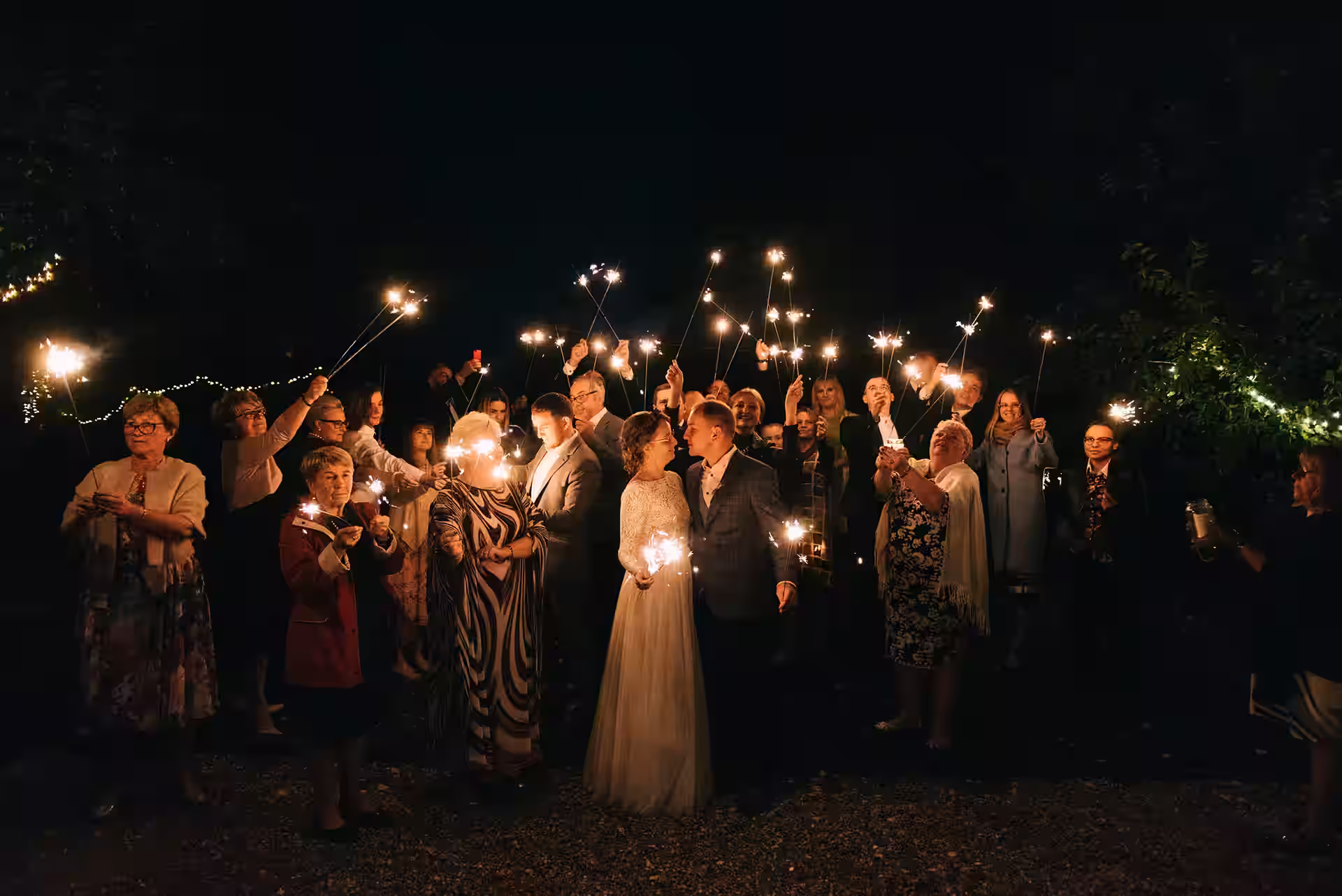 Para młoda i goście weselni z zimnymi ogniami – nocna celebracja wśród światełek i radości.