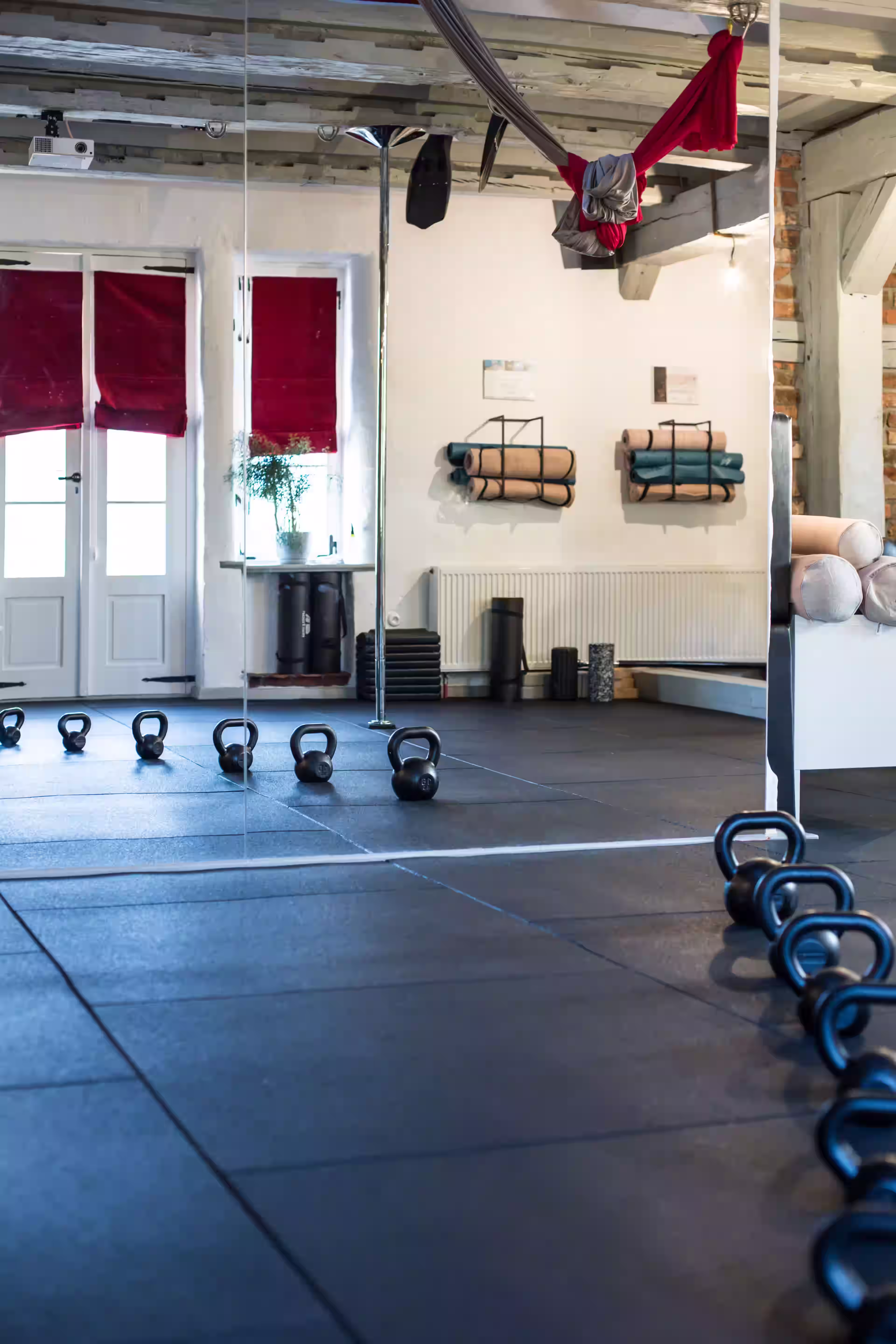 Wnętrze sali do jogi i treningu funkcjonalnego – hantle kettlebell, lustra, maty i hamak do aerial jogi.