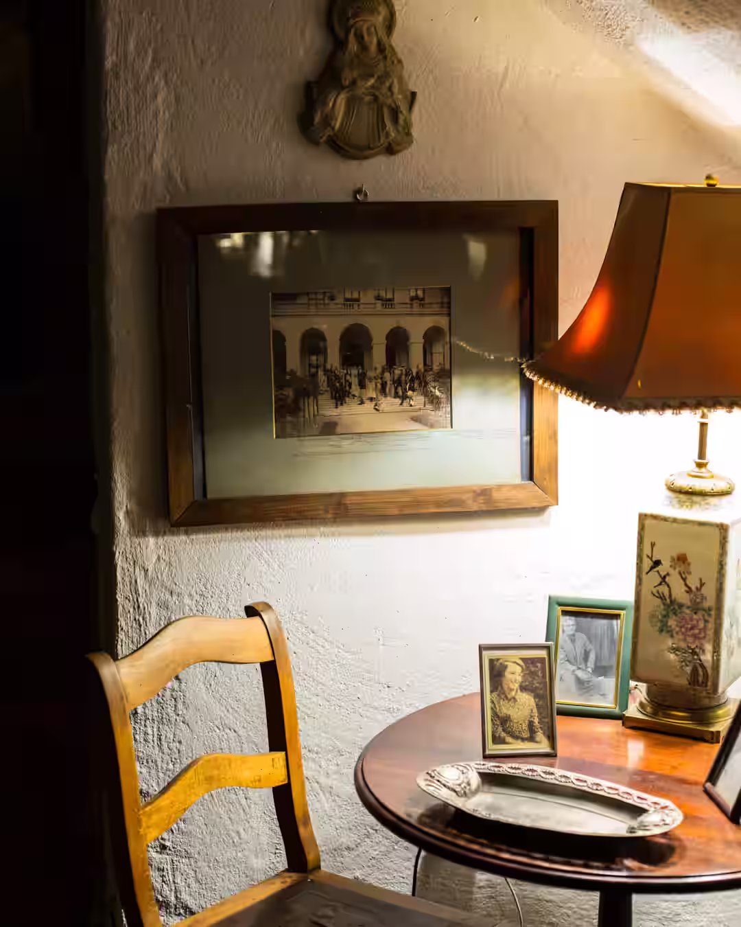 Kącik z lampą i rodzinnymi fotografiami – drewniany stolik, stare zdjęcia, obraz ślubny na ścianie.