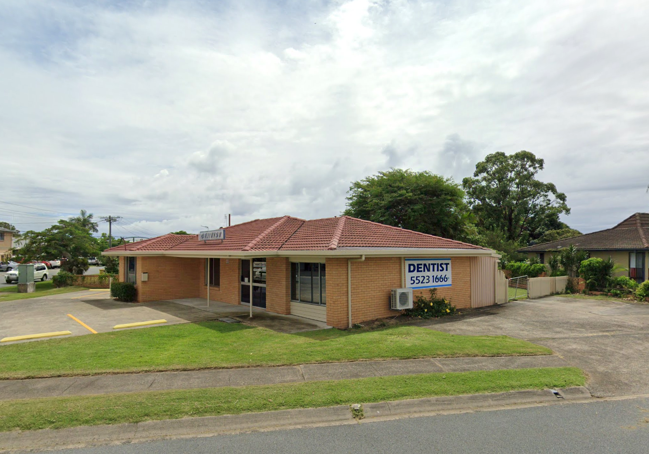 Single-storey brick dental clinic in Tweed Heads with red tiled roof, clear signage reading Tweed Dental | I Heart Smile, and surrounding greenery, photographed for I Heart Smile.