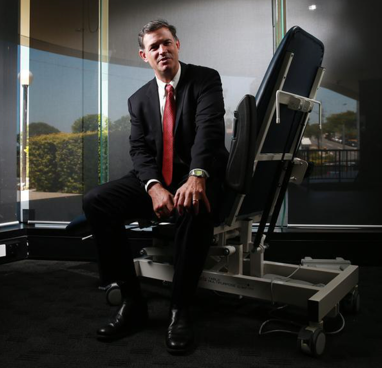 Dr. Christopher P. Hart seated beside a dental chair in a modern clinic setting, showcasing professionalism and expertise in dental care
