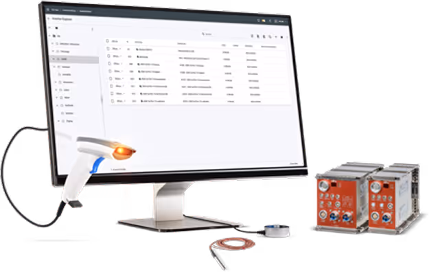 Computer monitor displaying inventory explorer software, a handheld barcode scanner with an orange light, and two electronic control modules on the right.