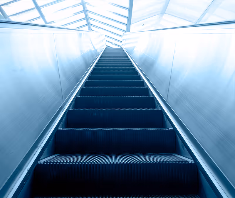 View looking up an empty escalator with bright overhead lighting and glass ceiling.