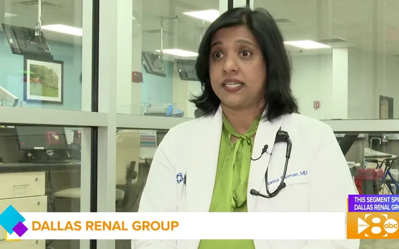 Female doctor in a white coat and green blouse speaking in a clinical office setting with glass walls.