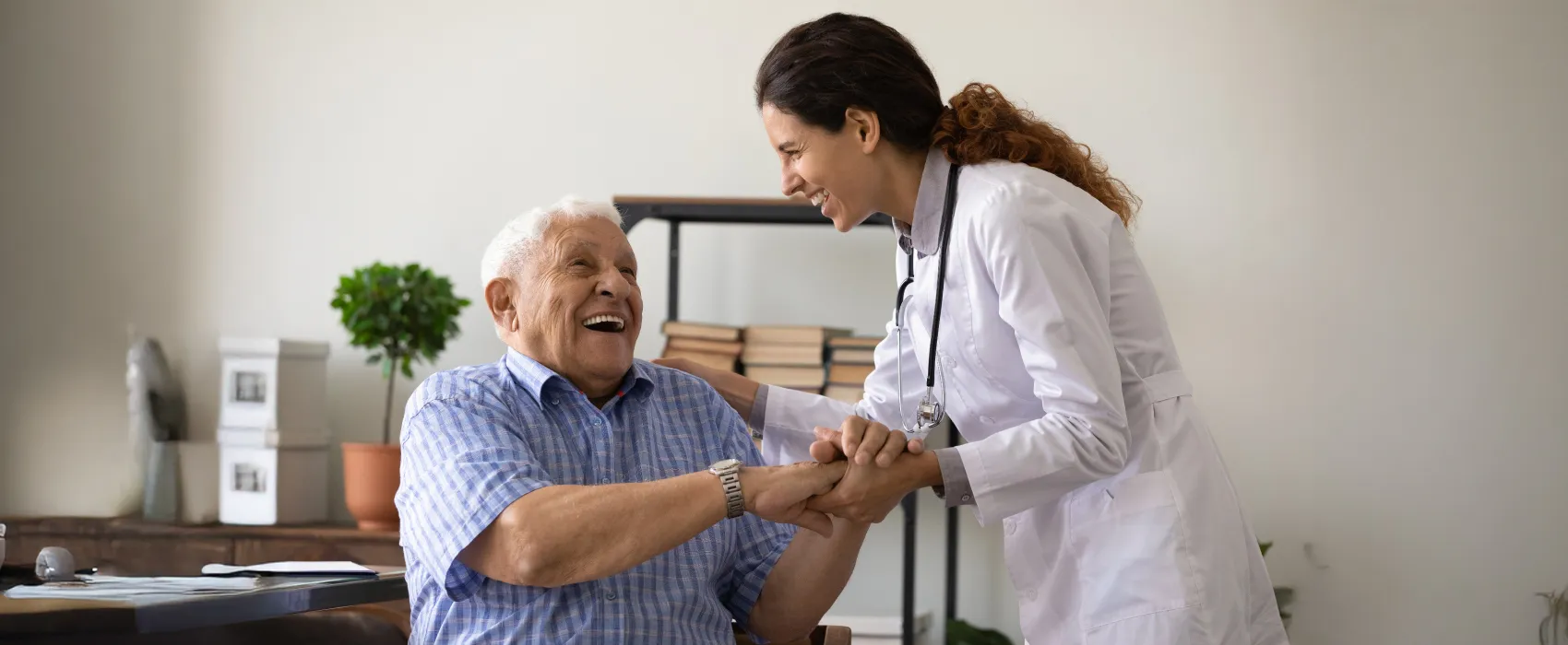 Smiling female doctor holding hands with a happy elderly male patient in a home setting.