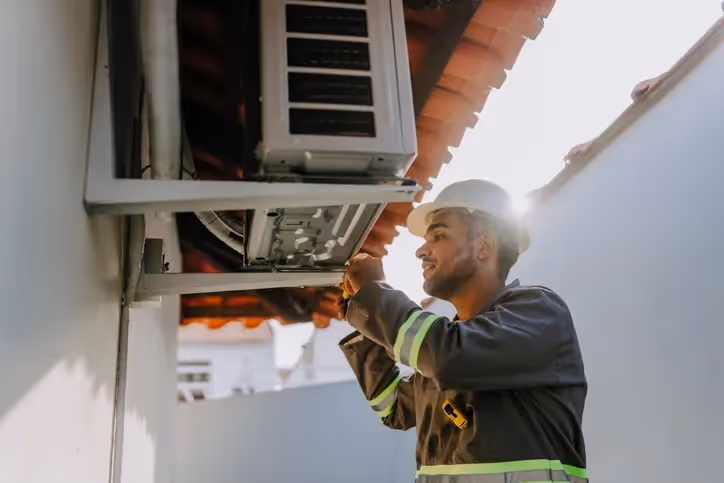 Man in hard hat installing outdoor AC unit.