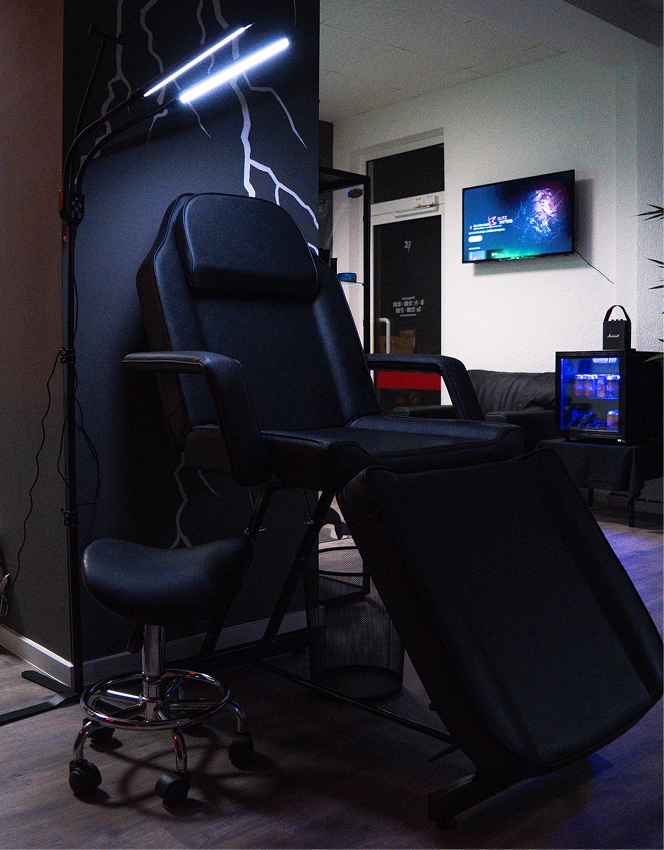 Black reclining chair and stool under bright lamp in a modern room with TV and mini fridge.