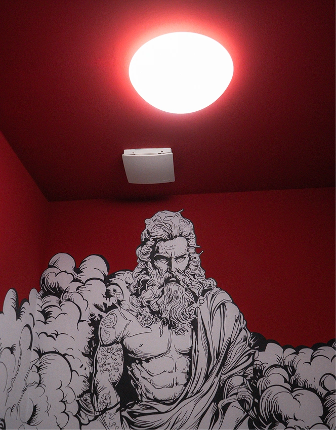 Black and white mural of muscular bearded man with tattoos on red wall under a bright ceiling light.