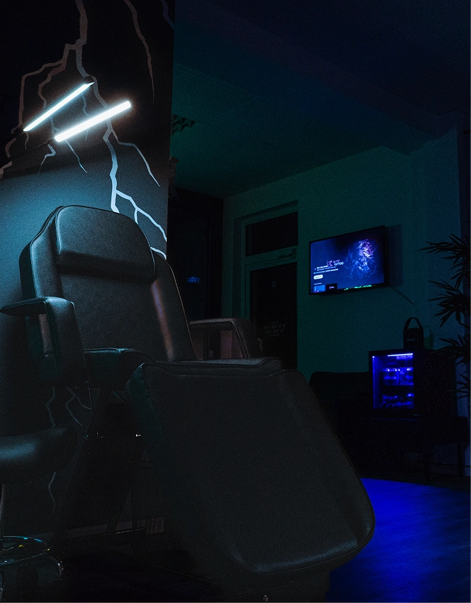 Black leather reclining chair in dimly lit room with neon wall lights and screen on wall.