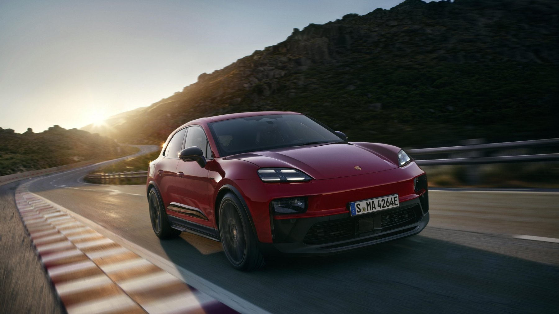 Porsche Macan GTS électrique rouge en mouvement sur une route de montagne au coucher du soleil