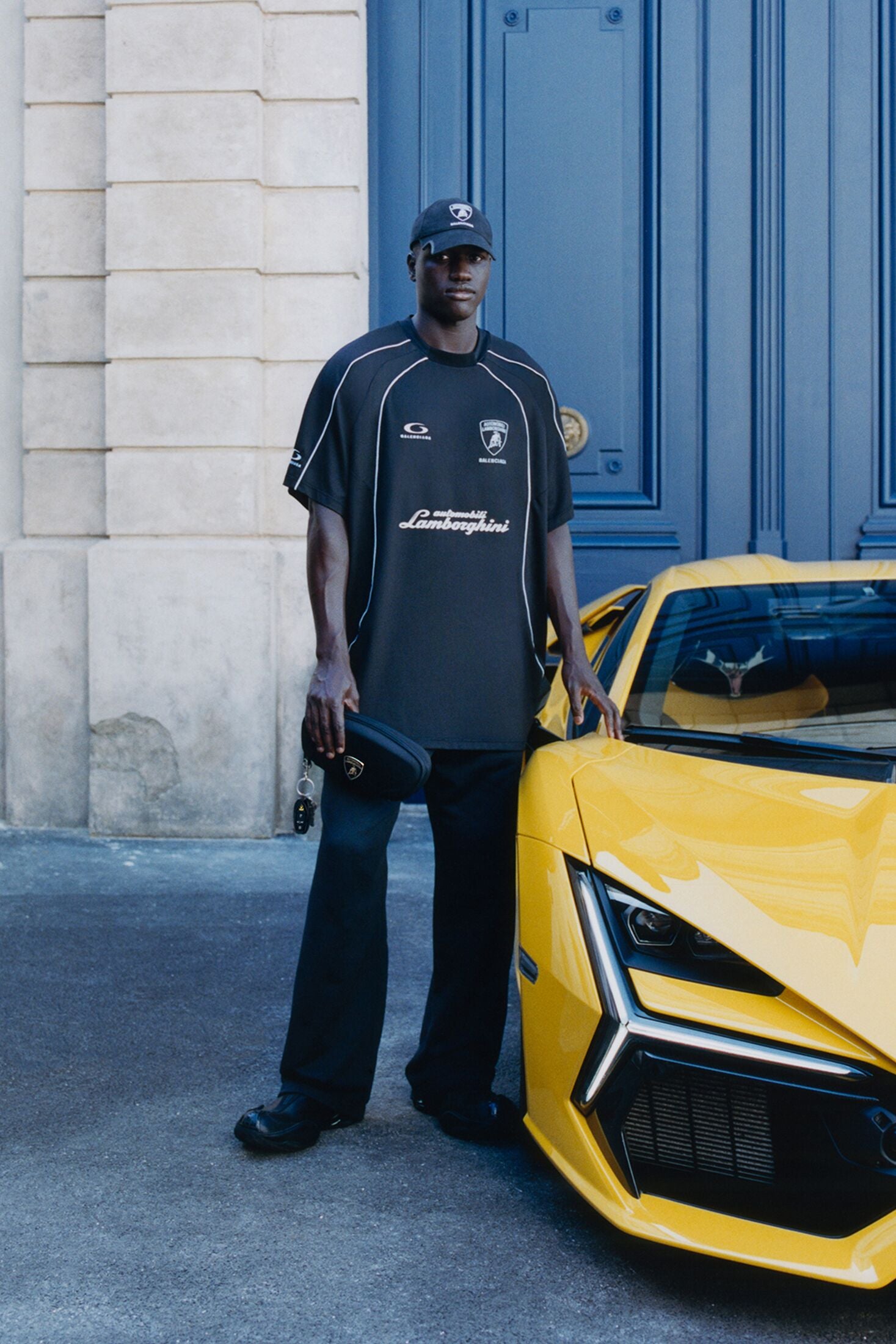 Look de campagne Balenciaga x Automobili Lamborghini (automne 25) à côté d’une Lamborghini Revuelto jaune