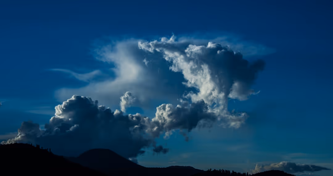 A cloudy blue sky with a mountain in the background.