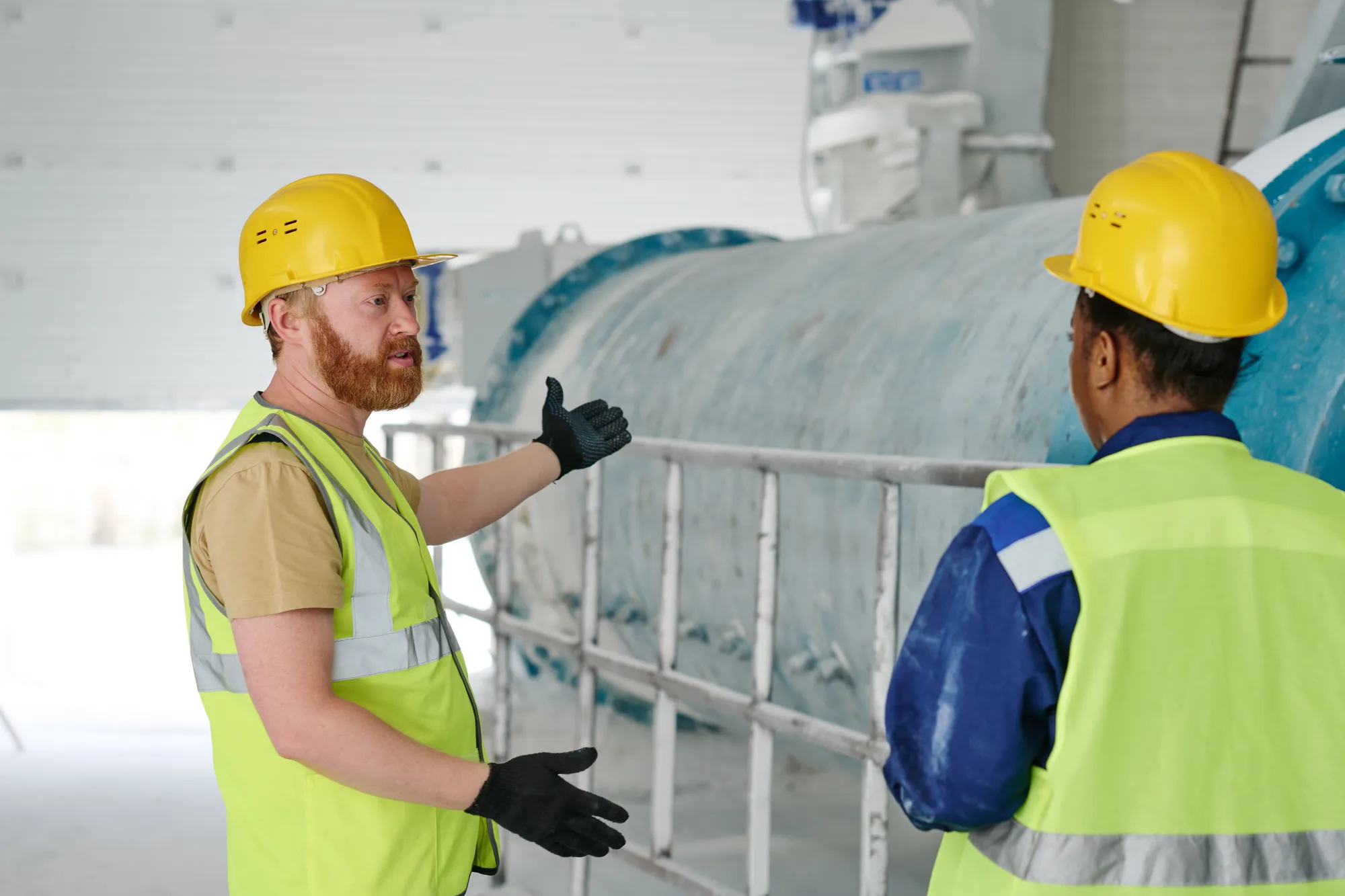 Two men wearing hard hats are standing in front of a large pipe.