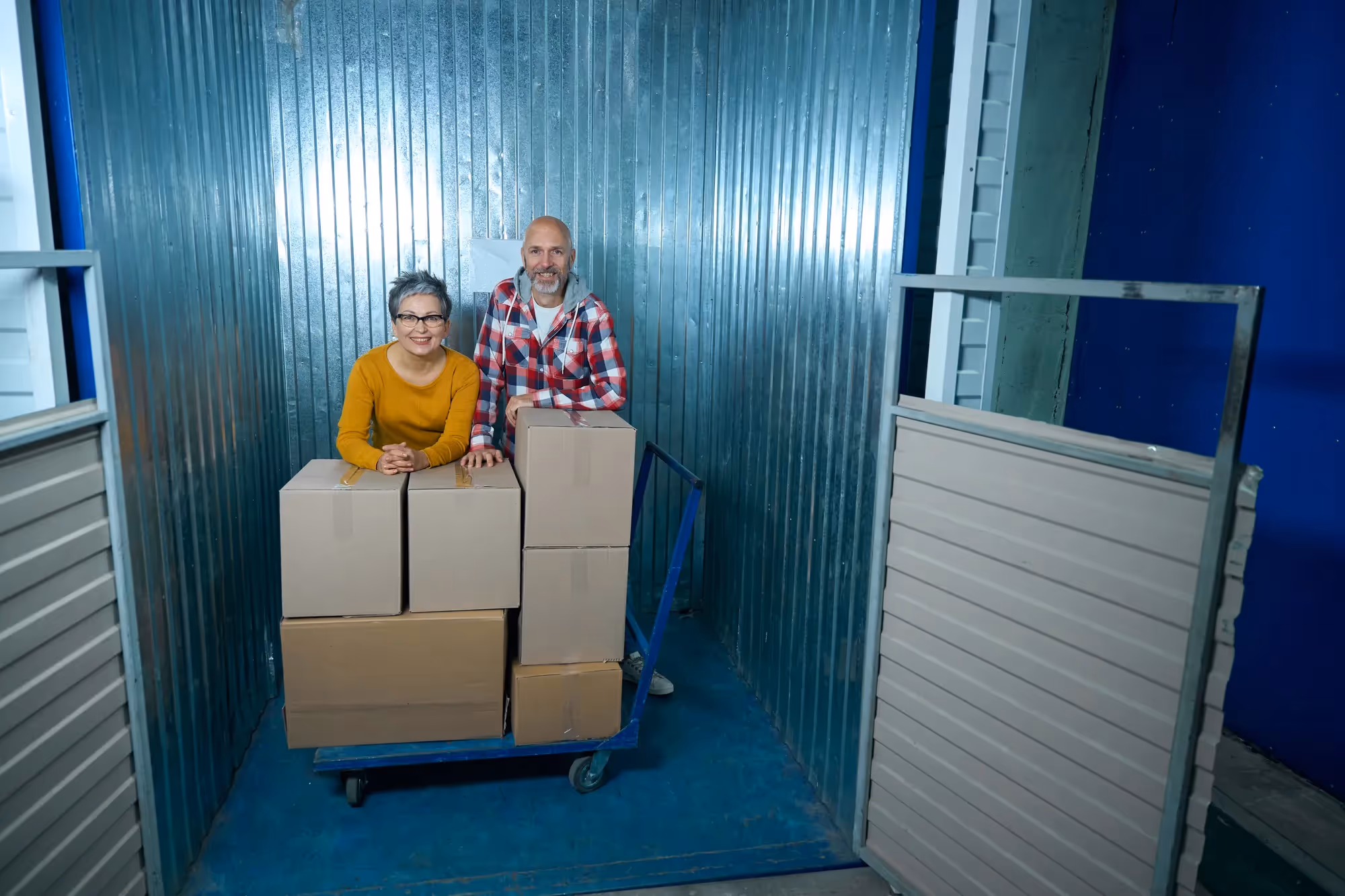 A man and woman standing in front of a blue wall with boxes.