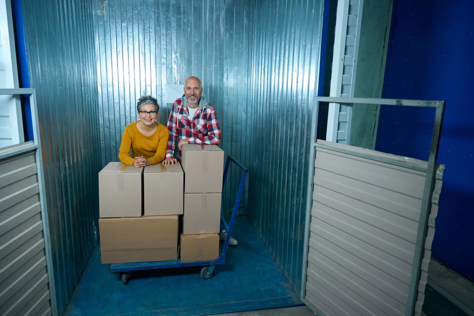 A man and woman standing in front of a blue wall with boxes.