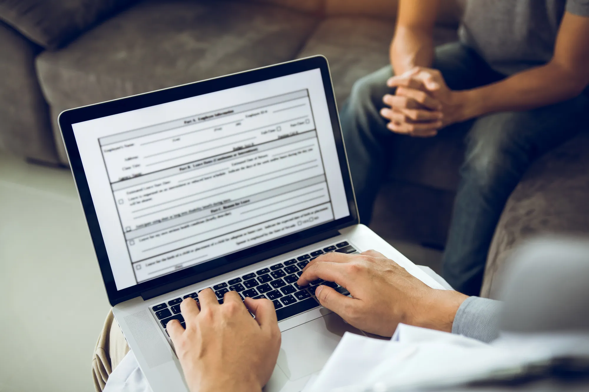A man is typing on a laptop with a form in front of him.