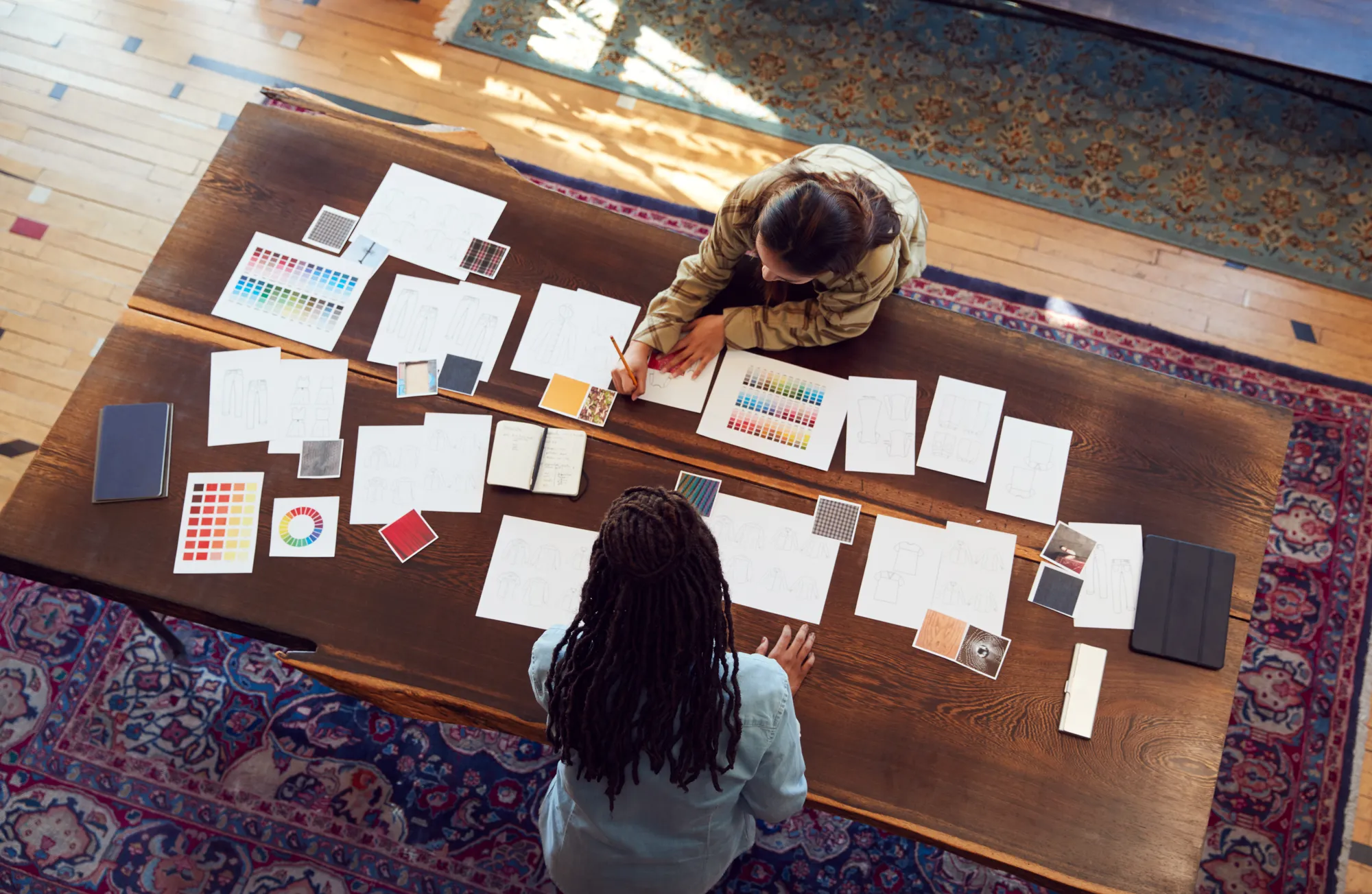 Two women sitting at a table with papers and a color wheel.