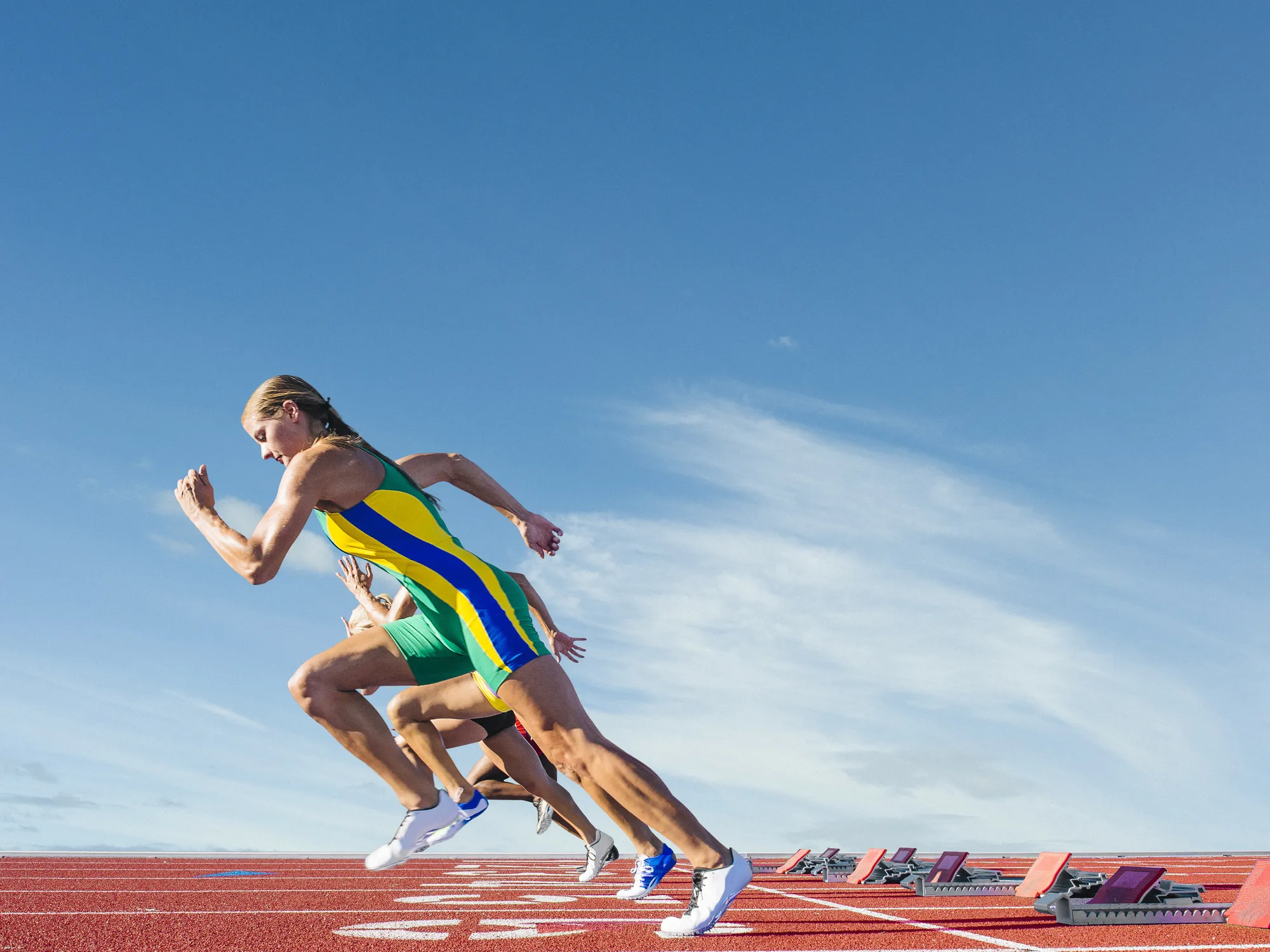 A woman running on a track with a blue and yellow jumpsuit.