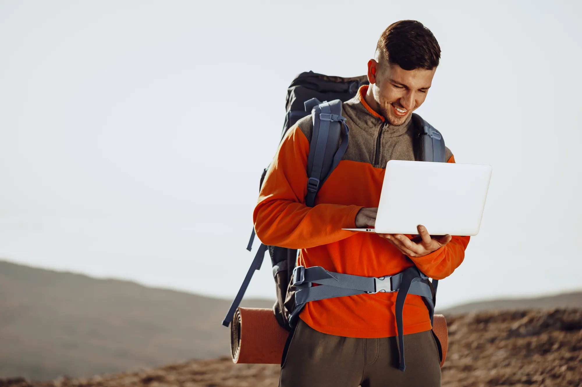 A man wearing an orange shirt and holding a laptop.