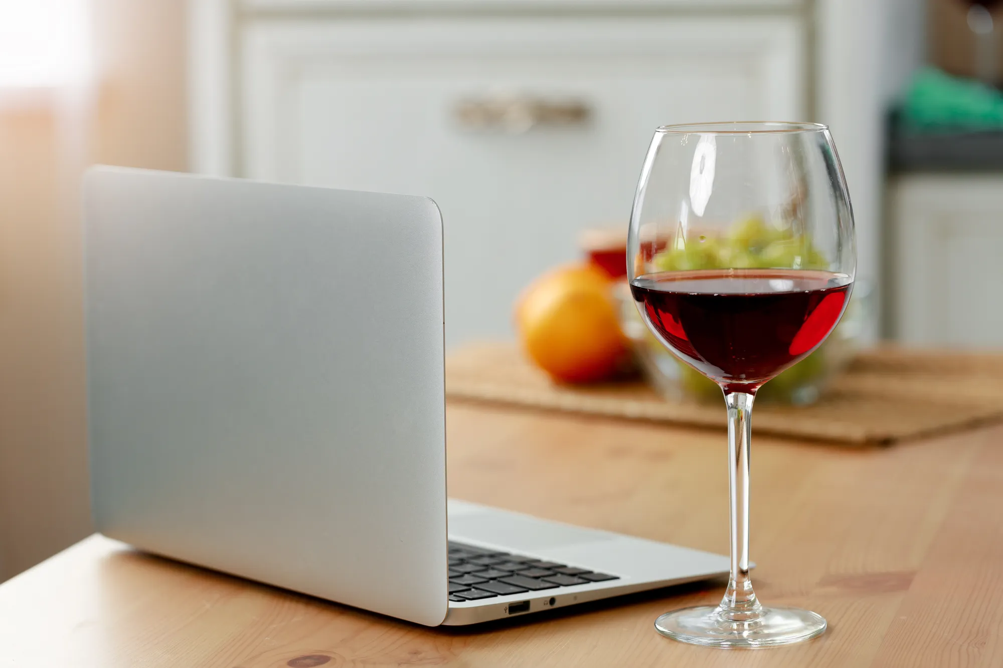 A laptop computer with a glass of wine on a wooden table.