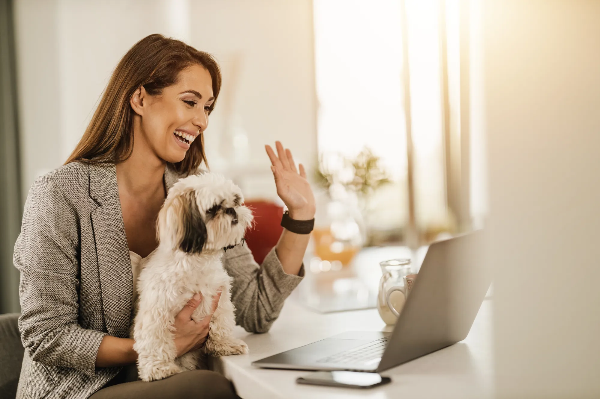 A woman holding a small dog while using a laptop.