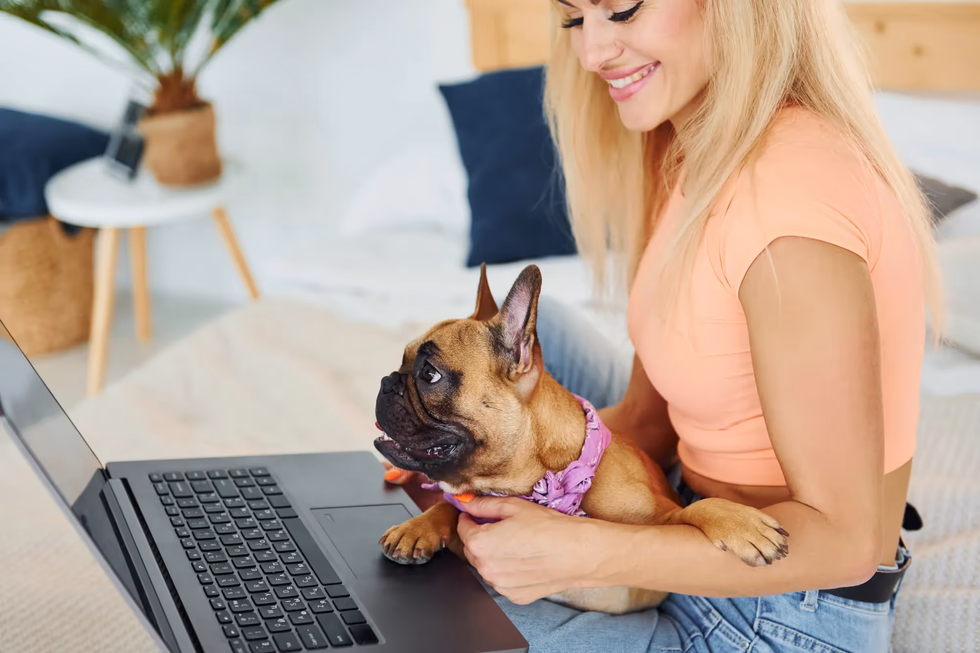 A woman holding a small dog in front of a laptop.