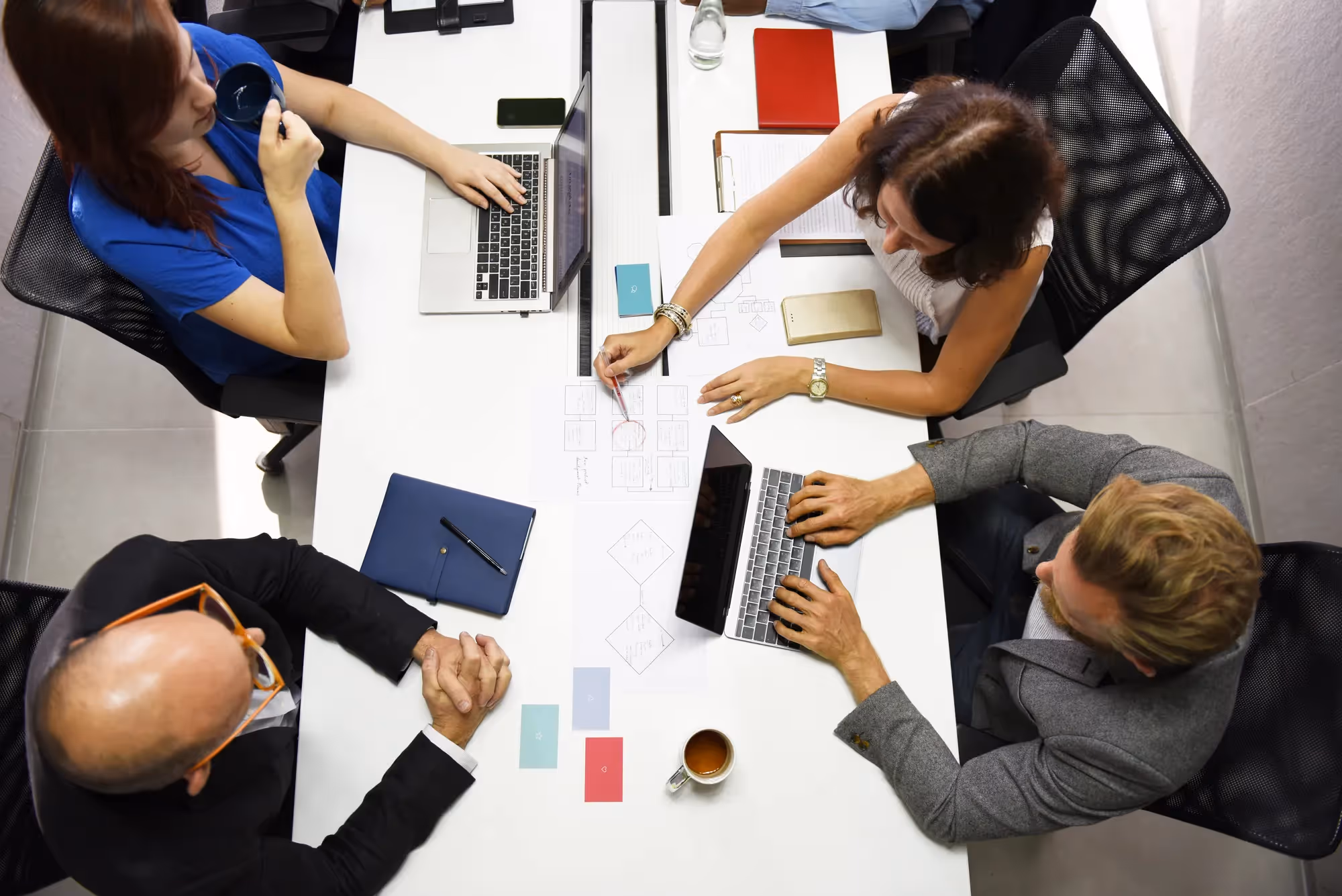 A group of people sitting around a table with laptops and a cup of coffee.