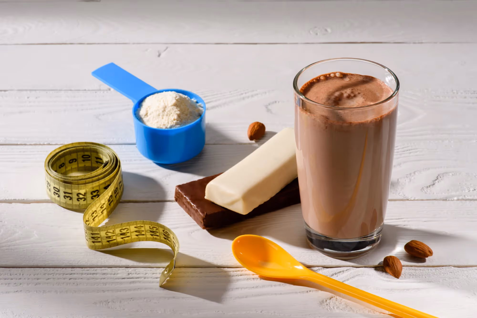 A glass of chocolate milk with a spoon and a cup of powdered milk.