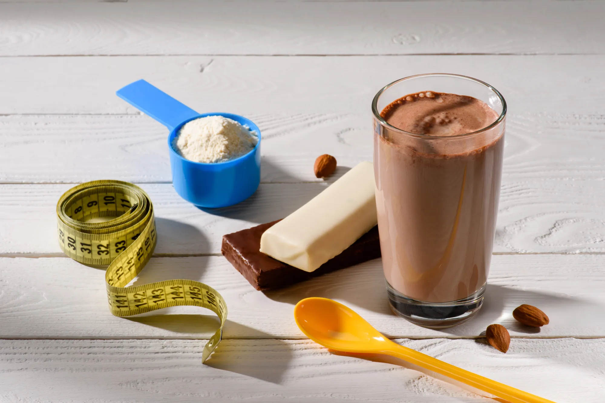 A glass of chocolate milk with a spoon and a cup of powdered milk.